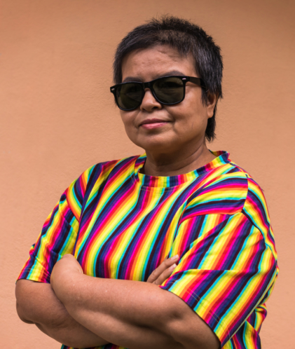 Androgynous close up portrait of Asian Middle-aged person posing standing with arms crossed in front of rainbow shirt